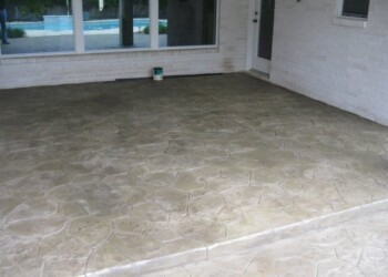 Stamped overlays on a concrete patio in front of a house in Eads, Tennessee. Stamped concrete patio with a textured stone pattern in front of a house.