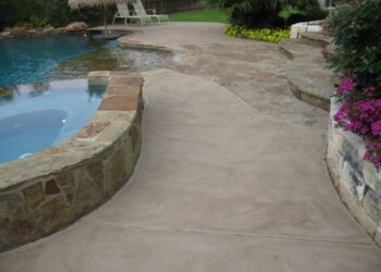 Stamped overlays on concrete patio near pool and garden in a residential backyard. Stamped concrete patio with a pool and garden in a residential backyard.