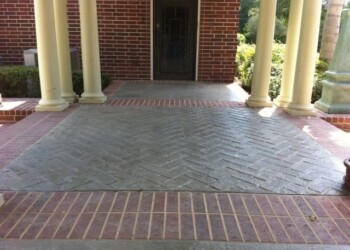 Stamped overlays on the porch with brick border and columns at a residential property. Stamped concrete porch with brick border and columns at a residential home.