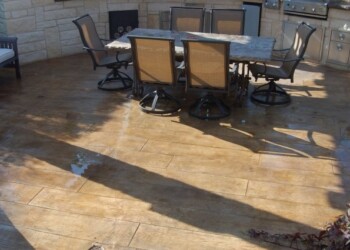 Outdoor dining area with stamped concrete surface in a backyard. Stamped concrete patio with outdoor dining table and chairs in sunlight.