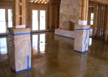 Finished acid-stained concrete floor with stone fireplace in a home under construction. Interior of a home with acid-stained concrete floor and stone fireplace under construction.