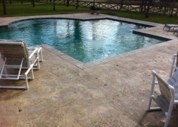Stamped concrete pool deck with chairs and a backyard fence. Stamped concrete pool deck with chairs and a backyard fence.