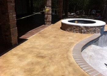 Stamped concrete patio with a hot tub in a backyard, featuring a curved design and decorative border. Stamped concrete patio with a hot tub and curved design in a backyard.