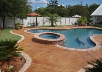 Acid-stained concrete pool deck with hot tub in a residential backyard in Eustis. Concrete pool deck with acid-stained finish and hot tub in a backyard with trees and a white fence.