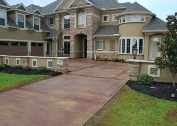 Finished acid-stained concrete driveway leading to a large house in a residential area. Exterior view of a large, multi-story house with acid-stained concrete driveway in a residential neighborhood.
