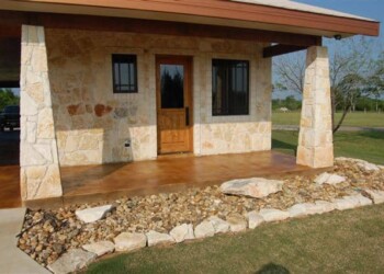 Concrete porch with acid stain finish at a home in a rural area. Exterior view of a stone and wood porch with acid stained concrete floor in a residential yard.