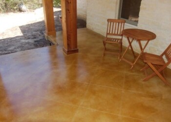 Finished exterior acid stained concrete patio with outdoor furniture in a residential area. Exterior acid stained concrete patio with wooden chairs and table in a residential setting.