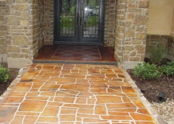 Stamped concrete walkway with a brick pattern leading to a black front door. Stamped concrete walkway leading to a black front door with glass panels.