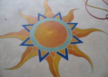 Vibrant sun artwork painted on concrete, featuring orange and yellow rays with blue accents. Colorful sun design painted on concrete surface with orange, yellow, and blue details.