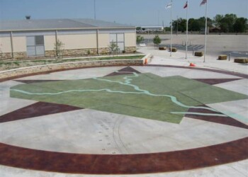 Concrete area with a painted map, parking lot, and flags in the background. Concrete outdoor area with a painted map and surrounding parking lot in a commercial area.