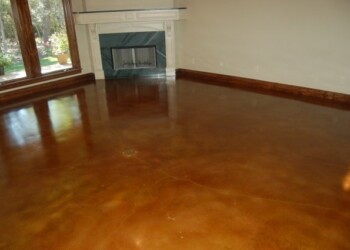 Interior acid stained concrete floor in a living room with fireplace and large windows. Finished interior concrete floor with acid stain in a living room with fireplace and large windows.