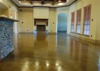 Living room with acid-stained concrete floor and large windows in a home in Eads, Tennessee. Interior of a spacious living room with polished concrete floor and a stone fireplace.