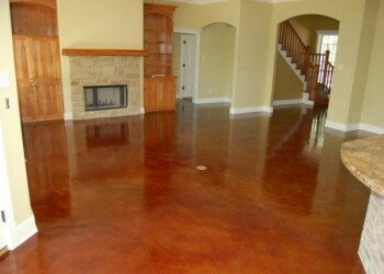 Polished acid-stained concrete floor in a living room with fireplace and staircase. Interior view of a living room with polished acid-stained concrete floor and a fireplace.