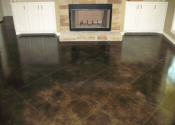 Finished acid stained concrete floor in a living room with fireplace and white cabinetry. Interior of a living room with dark stained concrete floor and white cabinets near a fireplace.