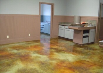 Interior acid stained concrete floor in a residential space, showing a mix of warm earth tones. Finished acid stained concrete floor in a room with beige walls and white cabinets.