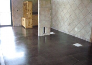 Concrete floor stained with acid, finished for a kitchen or dining area in Eads, Tennessee. Interior of a room with a dark stained concrete floor and tiled walls, showing a small wooden cabinet and a vent.
