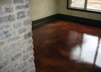 Finished acid-stained concrete floor in a room with large window and stone wall corner. Interior of a room with a polished acid-stained concrete floor and stone wall corner.
