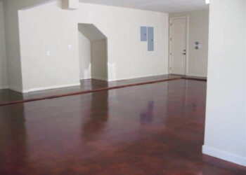 Finished interior with acid-stained concrete floor in a residential home. Empty room with polished hardwood floor and white walls in a house.
