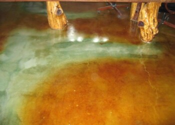 Interior acid staining on concrete floor with wooden table legs in a commercial setting. Colorful acid-stained concrete floor with wooden table legs in a commercial space.