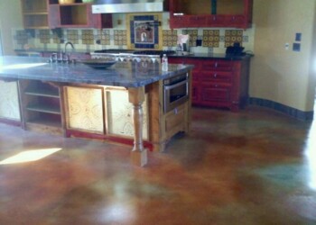 Polished concrete floor in a kitchen with red cabinets and colorful tile backsplash. Interior view of a kitchen with polished concrete floor and colorful tile backsplash.