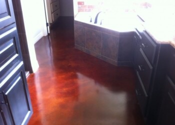 Interior acid stained concrete floor in a kitchen, showing a glossy finish and rich color. Polished concrete floor with a reddish-brown stain in a kitchen area.