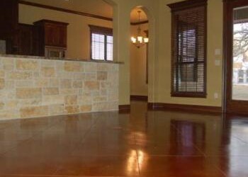 Polished acid-stained concrete floor in a living room with wooden blinds and a view of the dining area. Interior view of a room with polished acid-stained concrete floor and wooden window blinds.