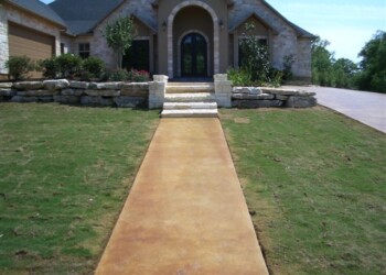 Concrete walkway with acid stain finish leading to the front steps of a house. Concrete walkway leading to a house with stone steps and landscaped yard.