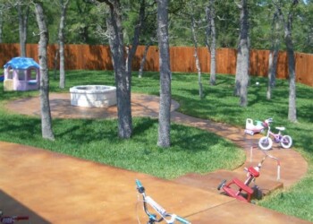 Finished concrete patio with children's play area in a backyard in Eustis, Florida. Backyard with trees, a wooden fence, and a concrete patio with children's toys.