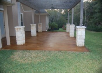 Finished concrete patio with stone pillars and pergola in a backyard in Euless, Texas. Concrete patio with stone pillars and a covered pergola in a backyard.