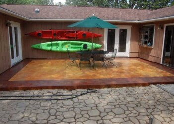 Acid-stained concrete patio with outdoor furniture and kayaks in the background. Patio with acid-stained concrete surface, outdoor table, chairs, umbrella, and kayaks on the wall.