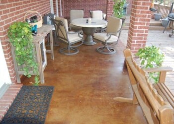 Exterior acid stained concrete patio with outdoor dining set and plants in a residential backyard. Finished exterior acid stained concrete patio with outdoor furniture and potted plants in a residential backyard.