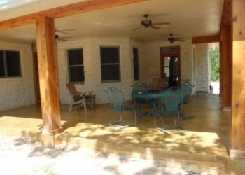 Outdoor patio with wooden beams, ceiling fans, and seating area in a backyard. Covered patio with wooden beams, ceiling fans, and outdoor furniture in a residential backyard.