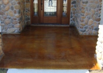 Finished concrete porch with acid stain in front of a wooden door and stone walls. Concrete porch with acid stain finish in front of wooden door and stone walls.