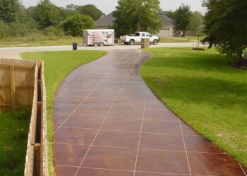 Concrete driveway with acid stain finish in a residential yard, with trees and a house in the background. Concrete driveway with acid stain finish in a residential yard, with trees and a house in the background.