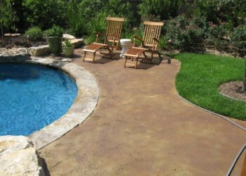 Concrete pool deck with acid stain finish and two wooden lounge chairs in a backyard. Concrete pool deck with acid stain finish and two wooden lounge chairs in a backyard.