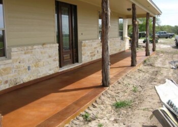 Exterior acid stained concrete porch with wooden posts in a residential yard. Concrete porch with acid stain finish and wooden support posts outside a house.