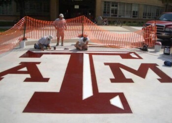 Workers painting the Texas A&M logo on a concrete surface at a job site. Workers painting a large Texas A&M University logo on a concrete surface.