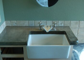 Granite countertop installed with a farmhouse sink in a kitchen. Kitchen sink with granite countertop and tile backsplash in a home.