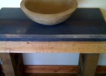 Wooden bowl placed on a black countertop in a rustic setting. Wooden bowl on a black countertop with a wooden frame in the background.