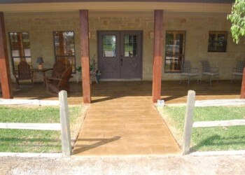 Stamped concrete walkway leading to the front door of a house in a residential neighborhood. Front porch of a house with stamped concrete walkway and outdoor seating area.