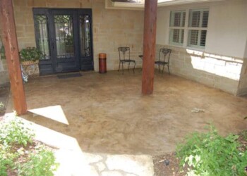 Stamped overlays on concrete patio in a residential backyard, with two chairs and support beams. Stamped concrete patio with seating area and support beams in a residential backyard.