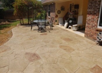 Stamped overlays on concrete patio with outdoor furniture in a Texas backyard. Stamped concrete patio with outdoor furniture and a covered porch in a residential backyard.