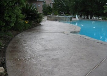 Stamped overlays applied to a pool deck in a residential backyard. Stamped concrete pool deck with a curved design in a backyard setting.