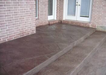 Stamped overlays on a concrete patio outside a brick house in Eads, Tennessee. Stamped concrete patio with brick house and white door in the background.