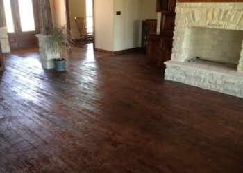 Stained concrete floor in a living room with fireplace and wooden furniture. Interior of a living room with stained concrete floor, fireplace, and wooden furniture.