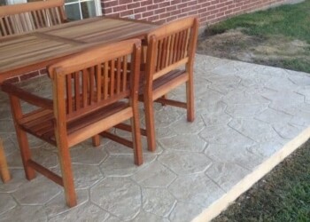 Outdoor dining set on stamped concrete patio in front of brick house. Wooden outdoor dining table with four matching chairs on stamped concrete patio.
