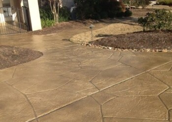 Stamped overlays on the driveway and walkway of a house in ECD Concrete, showing a natural stone pattern. Stamped concrete driveway and walkway at a residential property in ECD Concrete.