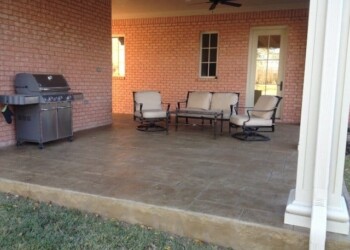 Outdoor patio with seating and grill in a residential backyard. Covered patio with outdoor furniture and a grill in a residential backyard.