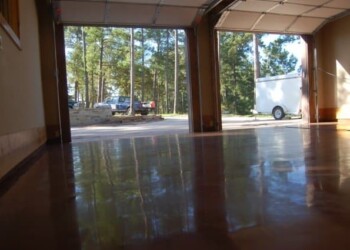 Polished concrete floor in a garage with open doors, view of trees and vehicles outside. Polished concrete floor inside a garage with open doors, showing trees and vehicles outside.