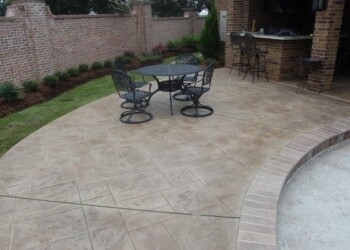Stamped concrete patio with outdoor table and chairs in a backyard. Stamped concrete patio with outdoor furniture and brick wall in the background.